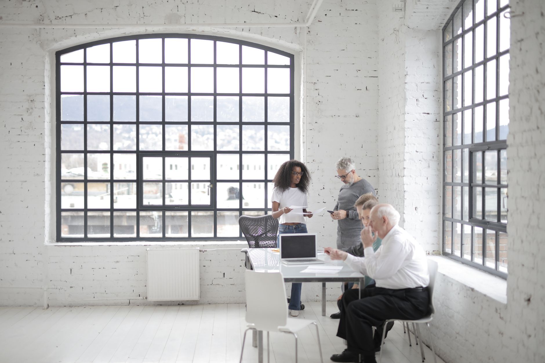 Lyst kontor med store vinduer og tre personer om et bord